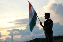 Silhouette of a Indian boy holding the Indian Tricolour flag celebrating the independence day.