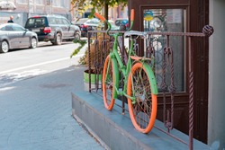 Colourful green and orange bicycle stands on the fence near entrance as a decoration. Decor. City. Style. Building. Outdoor. Urban. Shop. Cafe. Restaurant