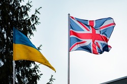 British and Ukrainian flags against the background of blue sky and spruce. Nature. Relationship. Diplomacy. Politics. Friendship. UK. Ukraine. Business. Agreement