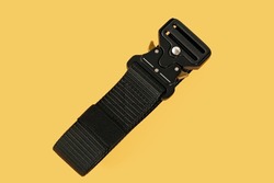 Subject shot of a black canvas belt fitted with a black metal male buckle and a black belt loop. The webbing belt is isolated on the orange background. Clothes. Utility. Textile. Special. Steel. Strip