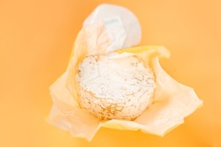 Open paper package of a whole head of camembert on an orange background. Soft cheese covered with edible white mold. Cream. Culinary. Meal. Object. Calories. Fat. Portion. Brie. Delicatessen