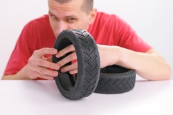 Man looks carefully at the tire threads of a small scooter tire on a white background. Wheel. Rubber. Black. Transportation. Vehicle. Tyre. Part. Repair. Good. Excellent. Fix. Fixed