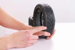 A male hand shows a pointing finger at the tire threads of a small scooter tire on a white background. Wheel. Rubber. Black. Transportation. Vehicle. Tyre. Part. Repair. Good. Excellent. Fix. Fixed