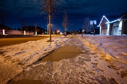 Ice and snow on a sidewalk at night with streetlight reflecting off the slick surface.