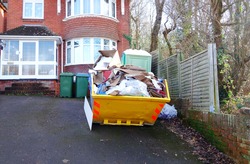 Big industrial rubbish bin in front of brick house with space to add text for background use, on side of heavy skip, driveway floor. Renovate, removal, recycle and home clearance concept.