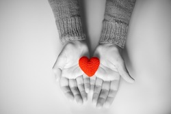 a person in a red sweater holds a red knitted heart in his palms. valentine's day holiday symbol. black and white photo