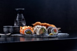Sushi and fried garlic shrimps, prawn on a stone plate with black background