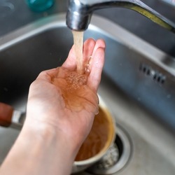Rusty orange water flows from the kitchen faucet onto a man's hand