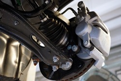 Close-up shows the suspension arm of a modern car in place of the connection with a ball joint and a brake caliper. Selected focus. Car service and auto parts.