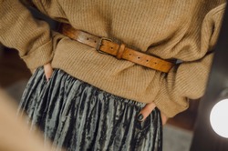 tender and beautiful women's hands touch the leather belt on the waist of a woman dressed in warm sweater and a long skirt. Concept for a women's store or showroom
