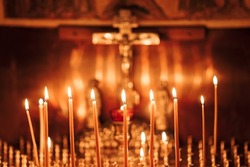 burning  candles in the temple, wax candles lit against the background of a cross with a crucifix, the concept of christian religion, prayers for the salvation of the soul, soft focus