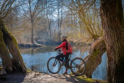 nice and active senior woman ring her electric mountain bike on a sunny day in early spring at river Enz in Baden-wuerttemberg, Germany