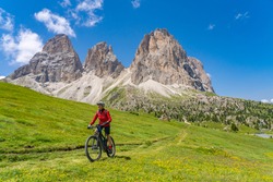 pretty beautiful senior woman riding her electric mountain bike below famous Sassolungo summit in Sella Dolomites  of Selva Wolkenstein, Val Gardena, South Tirol and Trentino, Italy