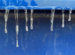 Many small icicles have frozen on blue trash can in the street in the winter.
