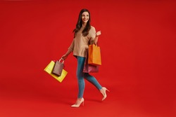 Full length of beautiful young woman in casual clothing carrying shopping bags and smiling