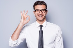 Everything is OK! Happy young man in shirt and tie gesturing OK sign and smiling while standing against grey background