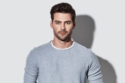 Handsome young man in casual wear looking at camera while standing against grey background