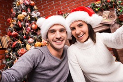 Capturing a happy moment. Beautiful young loving couple bonding to each other and smiling while making selfie with Christmas Tree in the background 