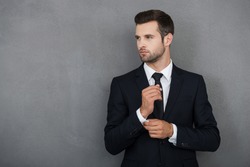 Perfect to the last detail. Handsome young businessman adjusting his sleeves while standing against grey background