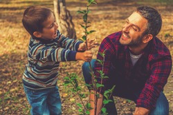 Planting a family tree. Happy young man planting a tree while his little son helping him