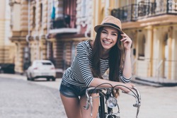 Funky beauty.  Beautiful young woman leaning at her bicycle and smiling while standing outdoors