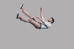 Man falling down. Mid-air shot of handsome young man falling against grey background 