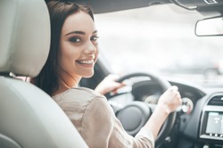 Confident and beautiful. Rear view of attractive young woman in casual wear looking over her shoulder while driving a car 