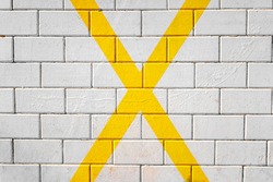 Large X shaped yellow cross painted on the pavement, background of a parking lot.