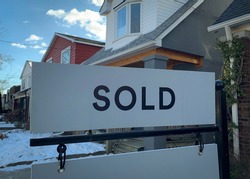 A real estate “sold” sign is seen in front of homes in the winter snow.