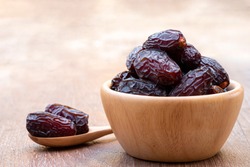 The large date fruits (Medjool) in cups and wooden spoons on a cement with blurred background.