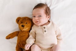 Smilling baby with a bear toy on the bed top view