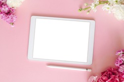 iPad pro tablet with white screen on pink color background with pen and flowers. Flatlay. Office background top view