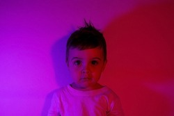 Boy child portrait in a white T shirt in neon purple light on the background of the wall, toddler boy violet light side view. High quality photo