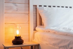 Vintage lamp near white bed in wooden house. Modern design apartment. Comfort home concept. Retro, vintage style. Interior design.