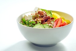 Delicious veggie bowl with cucumber, bell pepper, salad mix, quinoa and tofu in a white plate. Isolated on grey background.