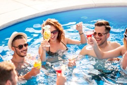 Group of friends having party in pool, drinking cocktail and enjoying together.