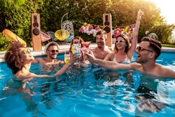 Group of friends having party in pool, drinking cocktails and enjoying together.