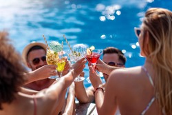 Friends drink cocktails by pool side on summer vacation and have fun together. People, love, summer, vacation and lifestyle concept.