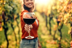 Woman tasting wine in vineyard. She is showing glass of wine to camera.