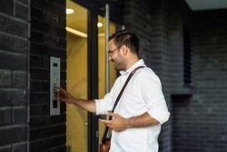 Young man using intercom at residential building entrance. People and business concept.