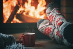 Girl resting and warming her feet by a burning fireplace in a country house on a winter evening. Selective focus