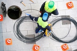 electrician workers installing optical fiber cable for internet and telephone underground lines  in city street