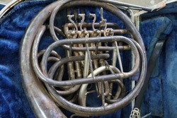 Close-up shot of an old silver French horn instrument, damaged instrument.