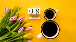 Two cups of coffee, a delicate bouquet of tulips and numbers. Greeting card for Women's Day on March 8. Fashionable yellow background. March 8 and the concept of 