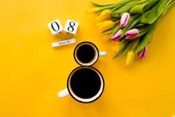 Two cups of coffee, a delicate bouquet of tulips and numbers. Greeting card for Women's Day on March 8. Fashionable yellow background. March 8 and the concept of 