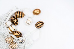 Gold, black, white Easter eggs in a string bag on a white background. Geometry. The minimal concept. Top view. Card with a copy of the place for the text.