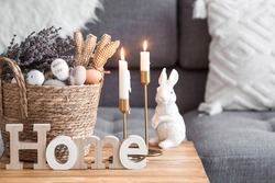 Provence. A wicker basket with Easter eggs, lavender, candles and white rabbits in the interior of the living room on a wooden table. The concept of home comfort in the bright holiday of Easter 2022.