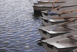 Several boats with oars are moored at the water's edge at the pier in the city park for water walks on the river, lake or pond.