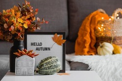 Cozy autumn concept. Home warmth in cold weather. Still-life. A blanket, pumpkins, flowers and the inscription home on the coffee table in the home interior of the living room.