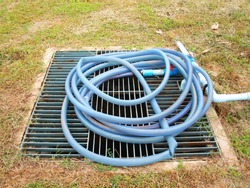 On the steel grating, the drain pipe cover has a rubber hose roll. On the lawn background in the footpath park